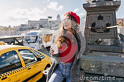 Stylish woman with cup of tea dreamy looking away in warm october day. Attractive white girl in beret posing with Stock Photo