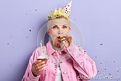 Stylish woman in party hat blowing noisemaker, celebrating birthday Stock Photo