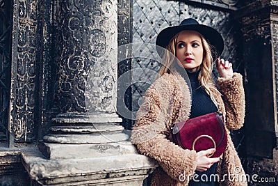 Stylish woman wearing teddy coat hat and holding red purse outdoors. Female fashion. Spring accessories. Clothes Stock Photo