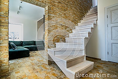 Stylish wooden contemporary staircase inside loft house interior. Modern hallway with decorative limestone brick walls and white Stock Photo