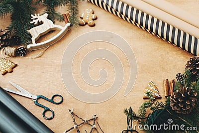 Stylish wrapping paper, wooden reindeer, gingerbread cookies, pine branches,cones, scissors, rustic thread on rural table, copy Stock Photo