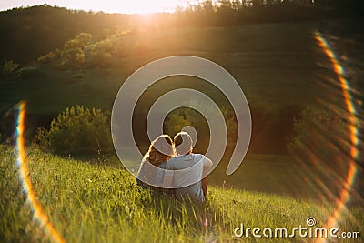Stylish young couple sitting on a hill and admiring the sunset. A film photo with a light and a sunlight, without a face Stock Photo