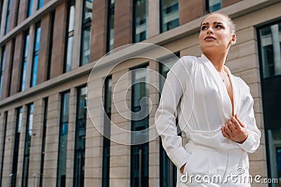 Stylish young European girl in a business suit. Caucasian lady looks to the side on a summer day against the backdrop of buildings Stock Photo