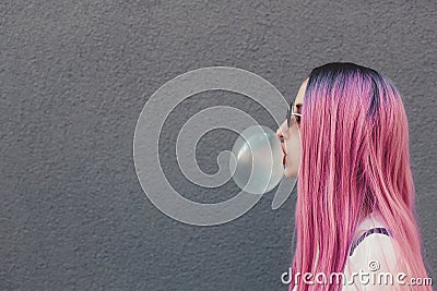 Stylish young hipster woman with long pink hair blowing a bubble with bubble gum. Stock Photo