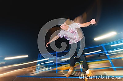 Stylish young skater in a fashionably tucked hat rides a skatepark at night. Night photo with the movement of lights and Stock Photo