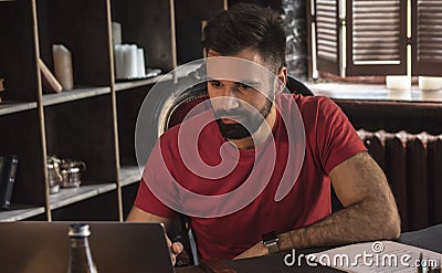 Young businessman with beard sitting in chair and working on laptop on table Stock Photo