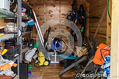 Suburban home wooden storage utility unit shed with miscellaneous stuff on shelves, bikes, exercise machine, ladder Stock Photo