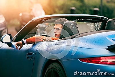 Succesful young adult handsome man drives luxury convirteble sport car at sunny day. Stock Photo