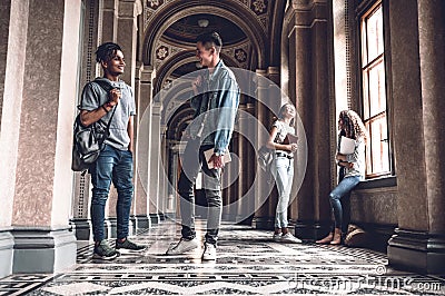 Success and knowledge helps us on the exam. Happy young students standing at the university hall and chatting Stock Photo