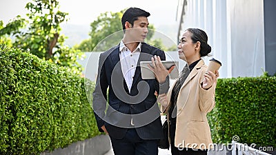 Asian male banker or businessman talking with aged businesswoman outside of the building Stock Photo