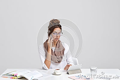 Successful busy prosperous businesswoman checks notes on touch pad while calls via smat phone, wears round glasses for Stock Photo