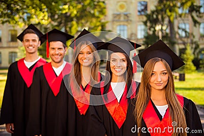 Successful confident five graduates in robes and hats with tassel smiling Stock Photo