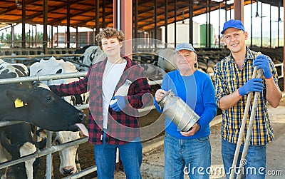 Successful elderly dairy farm owner with son and teen grandson standing in stall with cows Stock Photo