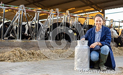 Female farmer posing with can of milk near stall with cows Stock Photo