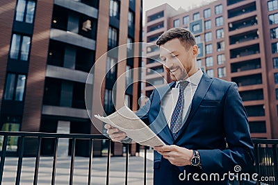 Successful happy young male economist reading article with financial news in morning newspaper Stock Photo