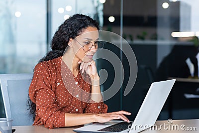 Successful Indian woman developer programmer working inside modern office, using laptop at work to write program Stock Photo