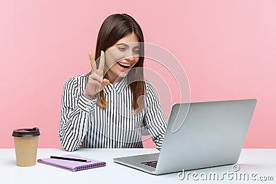 Successful positive woman office worker showing victory gesture and smiling looking into laptop screen, talking video call, online Stock Photo