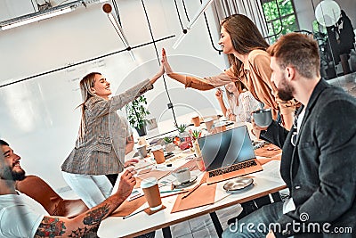 Successful project and two cheerful young business people giving high-five while their colleagues looking at them and smiling Stock Photo