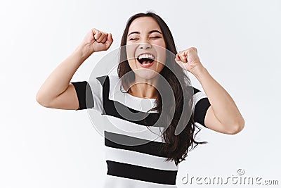 Successful, relieved young happy asian woman in striped t-shirt lifting hands up, fist pump like champion, feel lucky Stock Photo