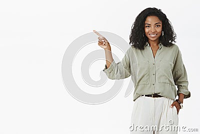 Successful stylish and happy dark-skinned businesswoman presenting project near chard holding hand in pocket pointing Stock Photo