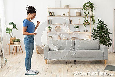 Excited Black Lady Weighing Standing On Weight Scales At Home Stock Photo