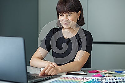 Successful woman plans work schedule, writes in notebook, sitting at workplace with laptop Stock Photo