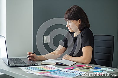 Successful woman plans work schedule, writes in notebook, sitting at workplace with laptop Stock Photo