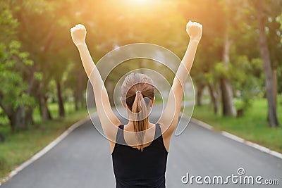 Successful woman raising arms after cross track running on summer sunset. Fitness female athlete with arms up celebrating success Stock Photo
