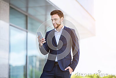 Successful young enterpreneur using cellphone for online communication near government office Stock Photo