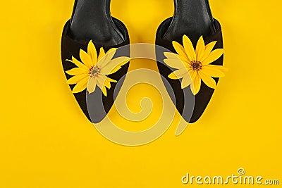 Suede black court shoes with yellow Topinambur flower bud on yellow background, womanhood concept Stock Photo