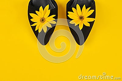 Suede black court shoes with yellow Topinambur flower bud on yellow background, womanhood concept Stock Photo