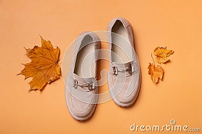 Suede woman's shoes with autumn leaves on orange background flat lay, top view. Stock Photo