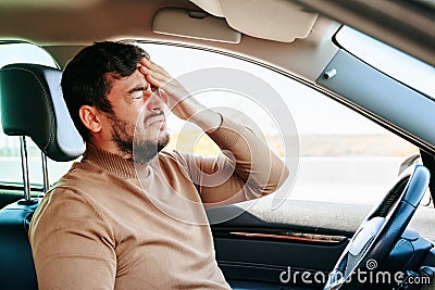Suffering guy young man is in the car and holds his hand on his head writhing in pain. Stock Photo