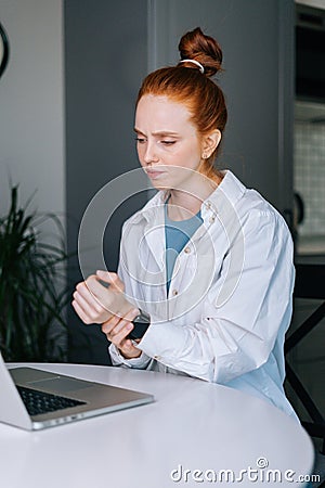 Suffering young redhead business woman having wrist pain during working at laptop computer Stock Photo