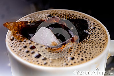 A sugar cube dropped into a cup with black coffee. Falling sugar into a warm drink Stock Photo