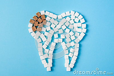 Sugar destroys the tooth enamel and leads to tooth decay. Tooth made of white and caries made of brown sugar cubes. Stock Photo