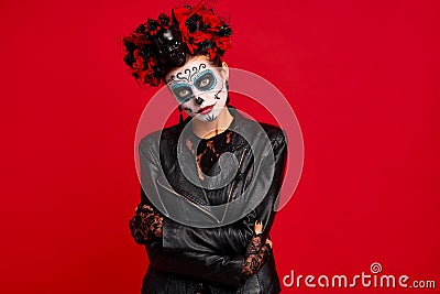 Sugar skull pretty girl with halloween makeup standing on bright red background. Wonderful female zombie with flowers in hair Stock Photo