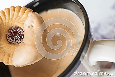 Sugared jam ring biscuit being dunked into frothy coffee in a mug Stock Photo