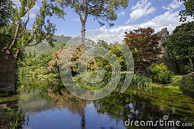 A suggestive landscape of the Garden of Ninfa in Italy with river, colored trees, plants and hills in the background. Editorial Stock Photo