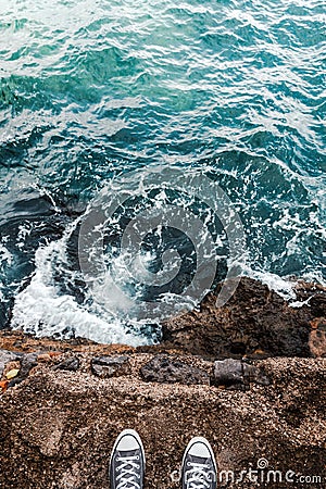 Suicidal ideation or thoughts, young person standing at the ocean cliff above the cold water and sea foam after waves crashing at Stock Photo