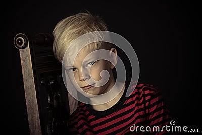 Sulky moody little boy sitting on a chair Stock Photo