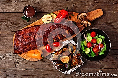 Summer BBQ ribs on a serving board with grilled vegetables, potatoes and salad over wood Stock Photo