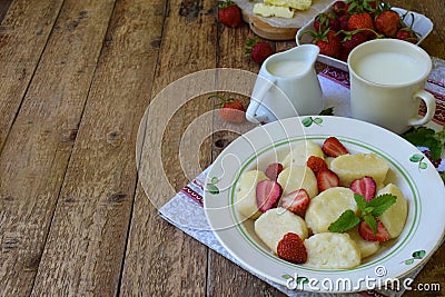 Summer berry breakfast. Sweet lazy pierogi, dumplings with sour cream, butter and strawberry on wooden background. Italian gnocchi Stock Photo