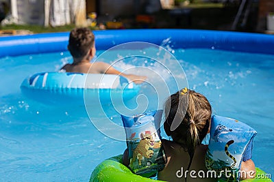 In the summer, children splash in the pool water on inflatable rings. Cute children swim in the blue water of an Stock Photo