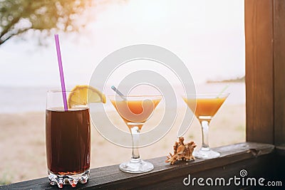 Summer concept: fresh exotic cocktails on wooden edge. Shell lying between glasses. Cola with straw and lemon. Island Stock Photo