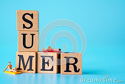 Summer concept : Minature people are taking sun bath on the SUMMER Word written on wooden cubes and a blue background Stock Photo