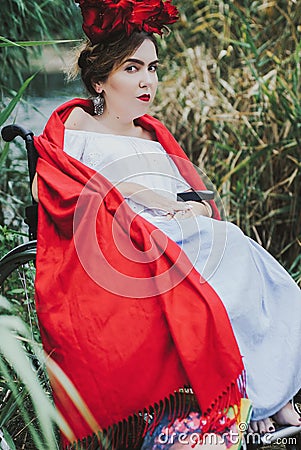 Conceptual portrait of beautiful young woman with red lips, red flowers in hair, sitting in wheel chair. Stock Photo