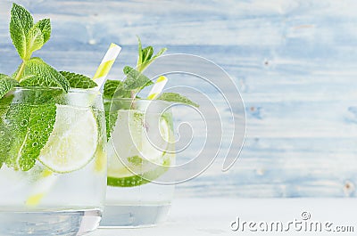 Summer cool lemonade in two wet glasses with mint, lime, ice, straw on vintage blue wood board, copy space, closeup. Stock Photo