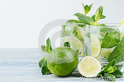 Summer cool lemonade in two wet glasses with mint, lime, ice, straw on vintage white plaster background, copy space, closeup. Stock Photo