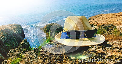 Summer details. A hat and sunglasses on a rock up close and blue sea in the background. Stock Photo